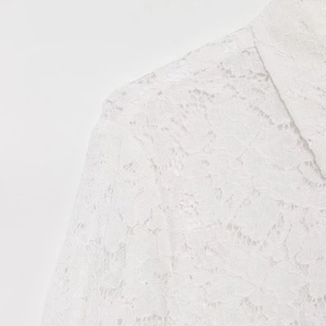 Close-up detail of elegant white lace shirt featuring intricate floral embroidery and seams