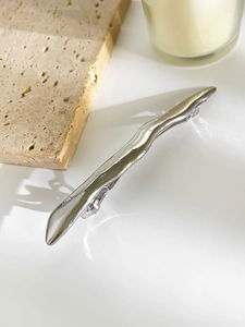 Detail of a wavy irregular silver metal hair clip with a polished finish on a white surface