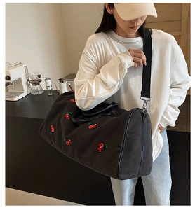 Detail of black canvas cylinder travel bag with red cherry embroidery and strap