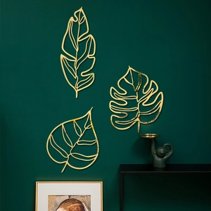 Lot de 3 décorations murales en métal doré avec feuilles évidées sur mur vert foncé