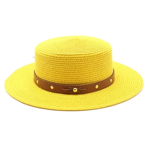 Détail d'un chapeau de paille jaune avec ruban en cuir marron et rivets dorés