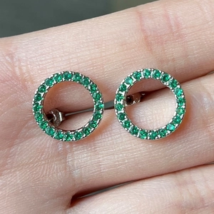 Minimalist silver circular stud earrings with green zircon pave setting held by hand