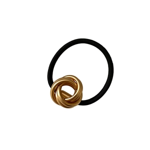 Minimalist black elastic hair tie with a decorative gold multi-loop metal knot accessory