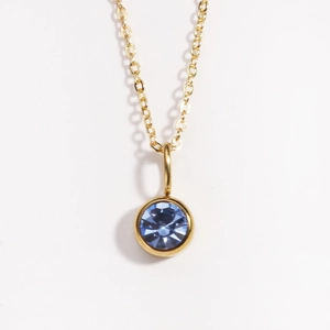 Macro focus on a gold necklace with a brilliant round faceted blue birthstone pendant