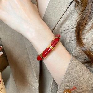 Detail of vintage gold bangle with red oval enamel inlay worn on model wrist