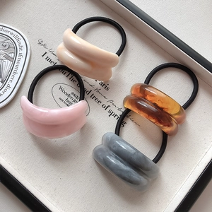 Macro detail of four acrylic marble pattern hair ties on a cream jewelry tray