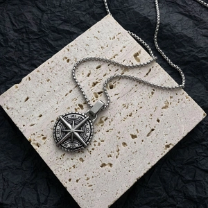 Star-patterned compass pendant necklace on a beige stone with a silver box chain