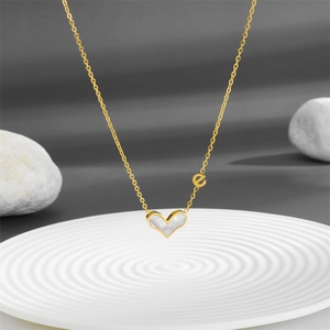 Golden heart necklace with white shell inlay and letter 'e' charm on a white plate