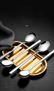 Set of four long handle stainless steel spoons displayed on a golden metal tray