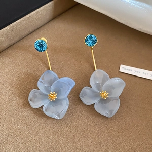 Close-up of elegant resin flower earrings with blue crystal studs and gold accents.