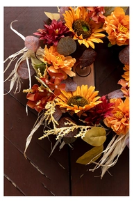 Close-up of artificial sunflower wreath with autumn leaves on rustic wood surface