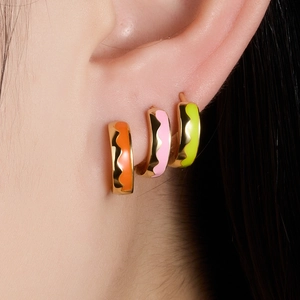Macro shot of colorful enamel wave earrings in orange pink and green on the ear