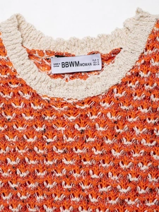 Detail shot of orange and white textured knit fabric with neckline brand tag showing size