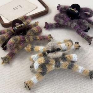 Detailed view of three knitted bow hair claws in purple, brown, and yellow stripes