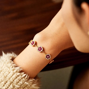Detail of 18k gold plated flower bracelet with red gems and crystals on model wrist