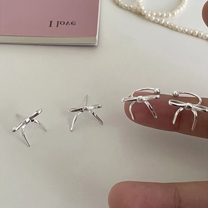 Elegant silver bow stud earrings and ear cuff set displayed on a soft aesthetic background