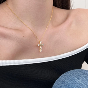 Close-up of golden cross pendant necklace with sparkling zircons worn by a model