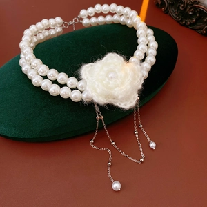 Macro detail of double-layer pearl necklace with plush white flower and silver tassels