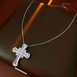 Macro shot of silver cross pendant with pink gemstones on a leather jewelry box lid