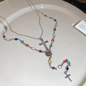 Close-up of a double-layered cross necklace featuring colorful gemstones and a vintage medallion