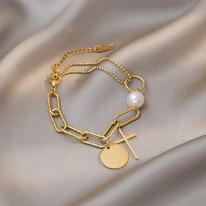 Gold titanium bracelet featuring pearl, cross pendant, and engraved round tag on silk