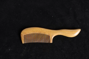 Detailed texture of green sandalwood comb with ergonomic handle on black background