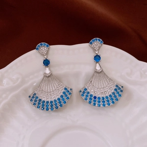 Close-up of fan-shaped silver earrings with blue stones on a vintage ceramic plate