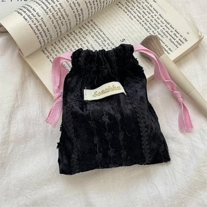 Detail of a black textured velvet drawstring pouch with pink silk ribbons and brand label