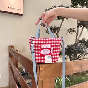 Detail of red checkered tote bag with denim handles and decorative patches in outdoor setting
