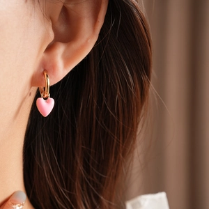 Close-up of a pink heart enamel charm earring with a gold hoop on a female model