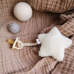 Detail of plush star pacifier clip in teddy velvet on textured muslin fabric background