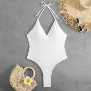 Flat lay of a white halter neck swimsuit with summer accessories on a textured background