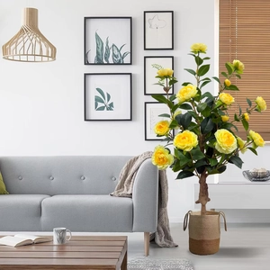 Detailed view of yellow artificial rose bonsai with green leaves in a woven basket