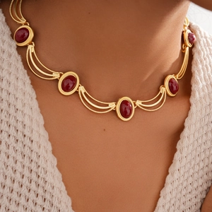 Gros plan d'un collier doré vintage avec gemmes rouges ovales sur un mannequin en maille