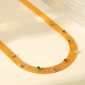 Golden mesh choker necklace with colorful gemstones on a textured glass background