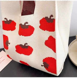 Close-up of a cream knitted tote bag featuring red and brown woven persimmon patterns