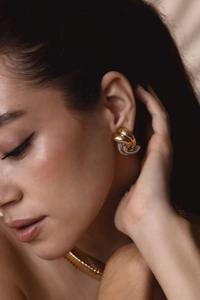 Close-up of model wearing two-tone gold and silver twisted knot stainless steel earrings