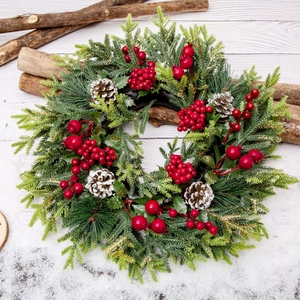 Christmas wreath with green pine needles, red berries, and frosted pinecones on white wood