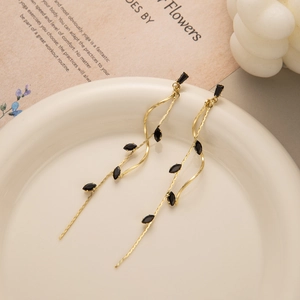 Close-up of elegant gold tassel earrings with black marquise gems on ceramic plate