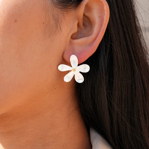 Silver flower stud earrings with brushed texture and golden center beads on ear