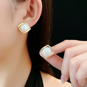 Gros plan d'une boucle d'oreille carrée dorée avec nacre blanche et petits cristaux
