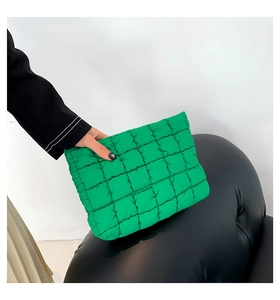 Close-up of a green quilted pleated clutch bag held by a hand on a black leather chair