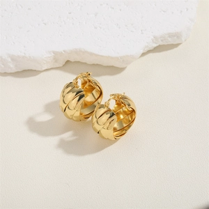 Macro detail of golden twisted hoop earrings on natural stone background