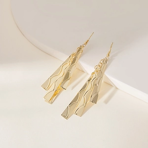 Detail of gold layered wave texture earrings on minimalist geometric pedestal