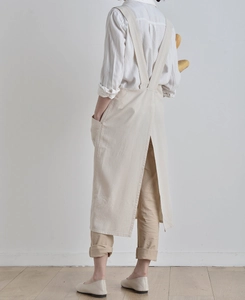 Detail of cross-back straps and side pocket on beige linen garden apron worn by a model