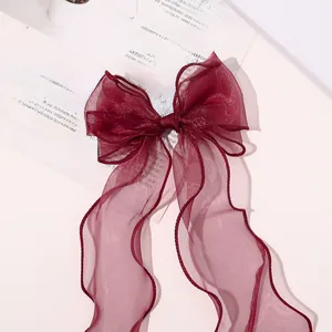 Close-up of elegant wine red organza bow hair clip with long ribbons on book background
