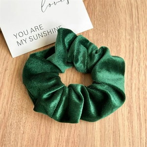 Close-up of deep green velvet scrunchie with ribbed texture on a wooden table