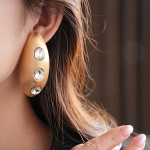 Close-up of gold oval brushed earrings with three inlaid rhinestones on a model