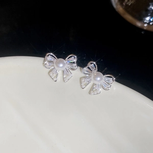 Macro detail of bowknot pearl earrings with glittering cubic zirconia stones and silver pins