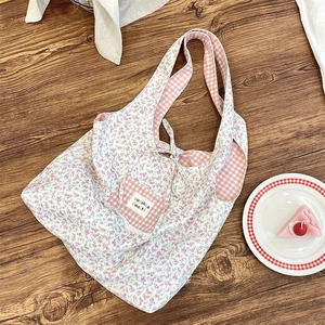 Detailed close-up of a floral canvas tote bag with pink plaid pocket on wooden desk